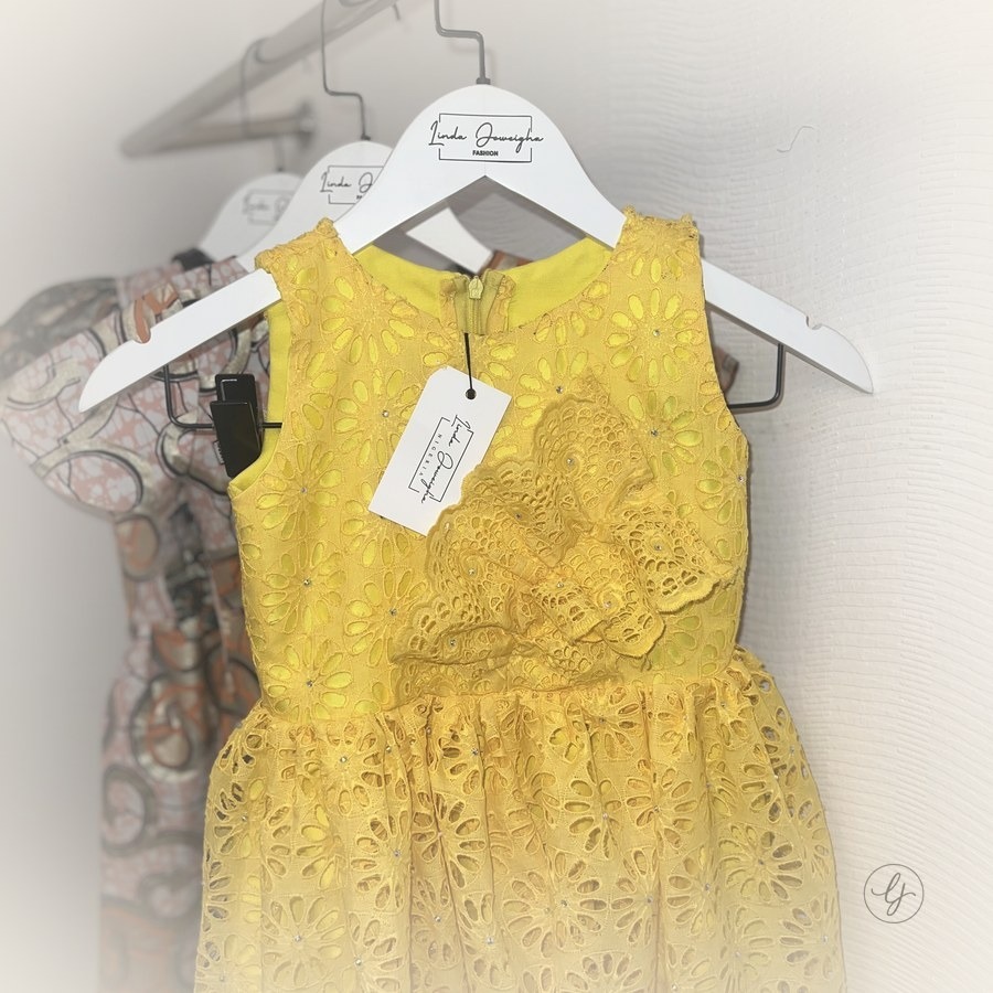 Yellow eyelet lace dress with rhinestone detailing on a hanger